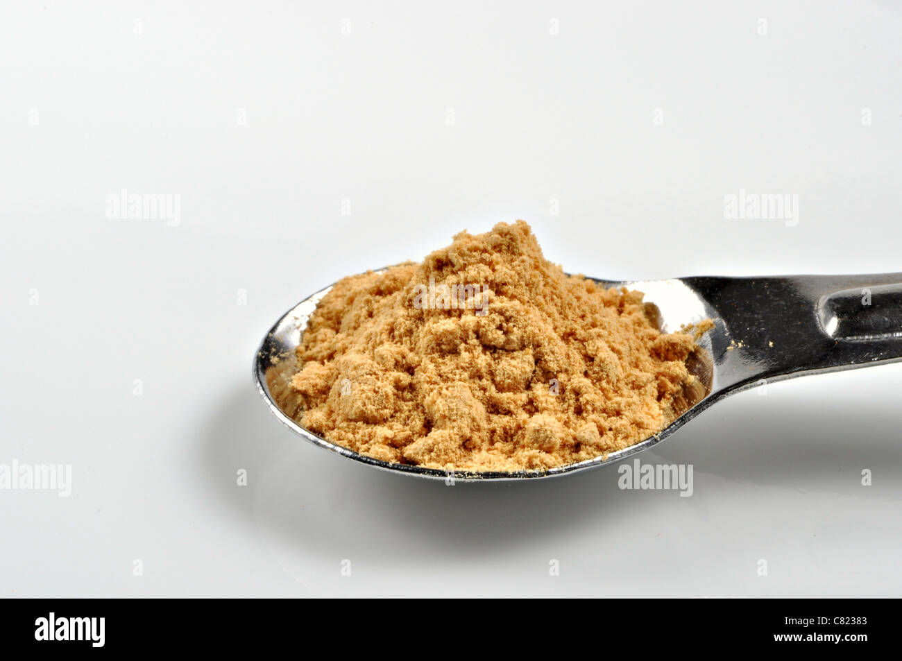 Gemahlener Ingwer sitzt in einem metallischen Dosierlöffel auf weißem Hintergrund. Stockfoto