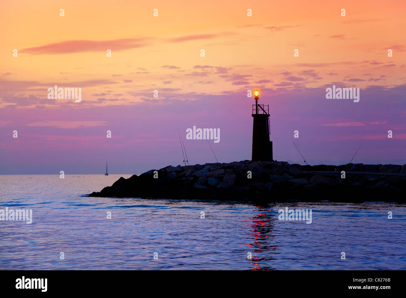 Sunrise-Leuchtturm im Meer lila und orange Himmel leuchten Stockfoto