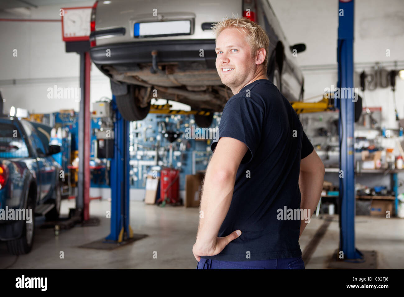 Glücklicher lächelnder Mechaniker in einer Autio Reparaturwerkstatt, schaut in die Kamera Stockfoto