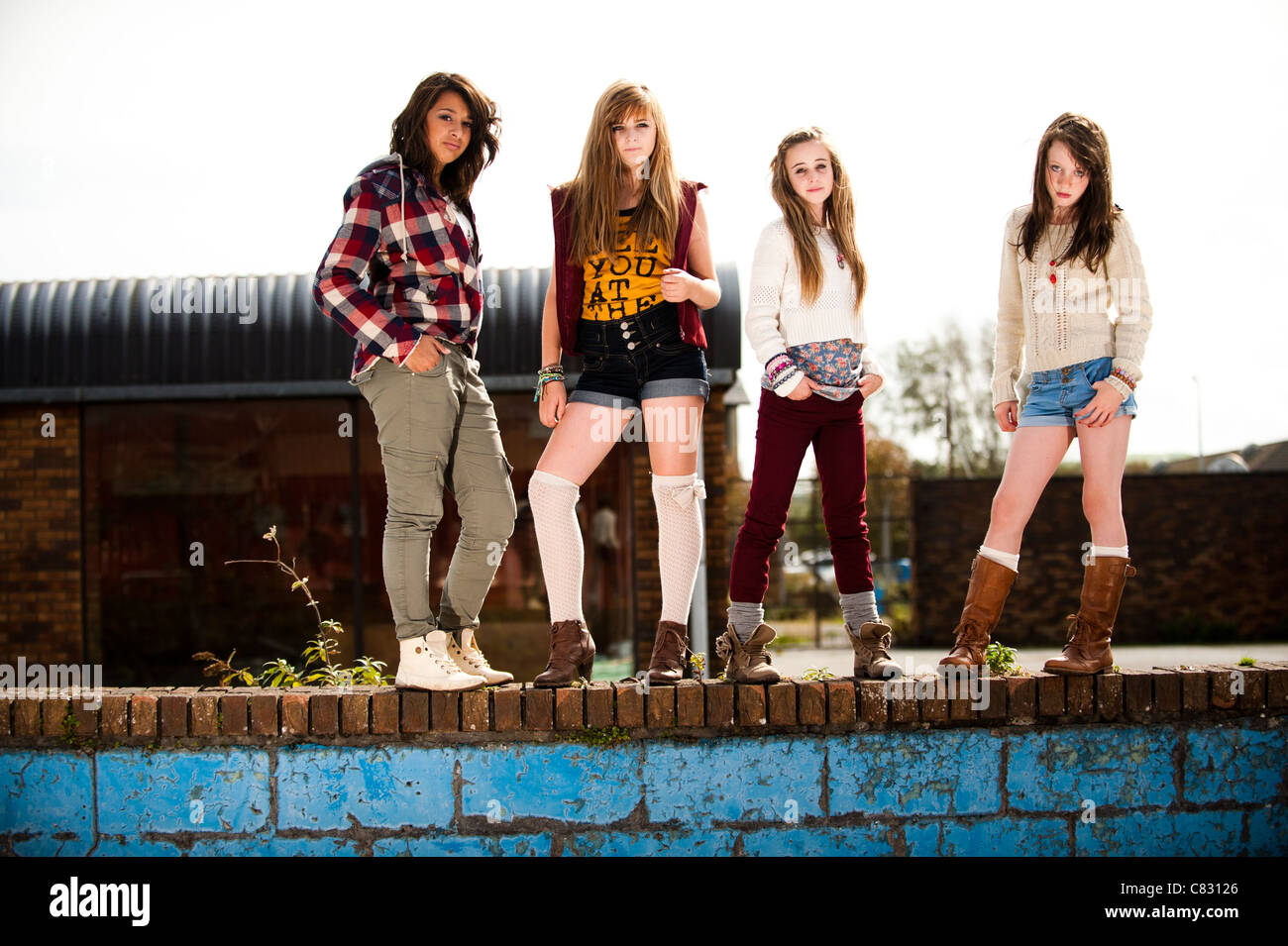 Eine Gruppe von 13 Jahre altes Mädchen im Teenageralter, launisch Haltung steht auf einer Mauer UK Stockfoto