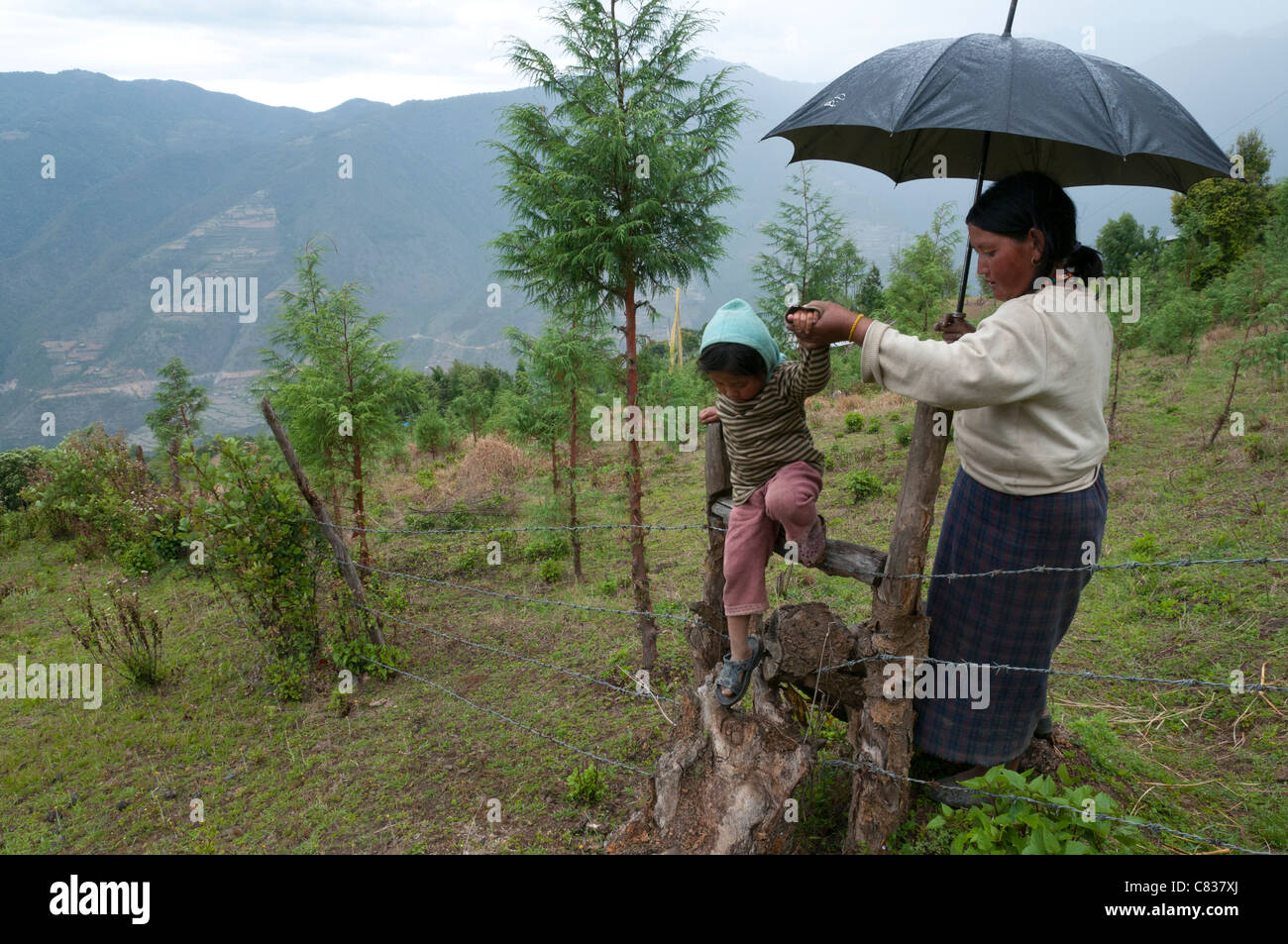 Bäuerin, die helfen, ihre Tochter Barb Wire Zaun zu überspringen. Radi. Ost Bhutan Stockfoto