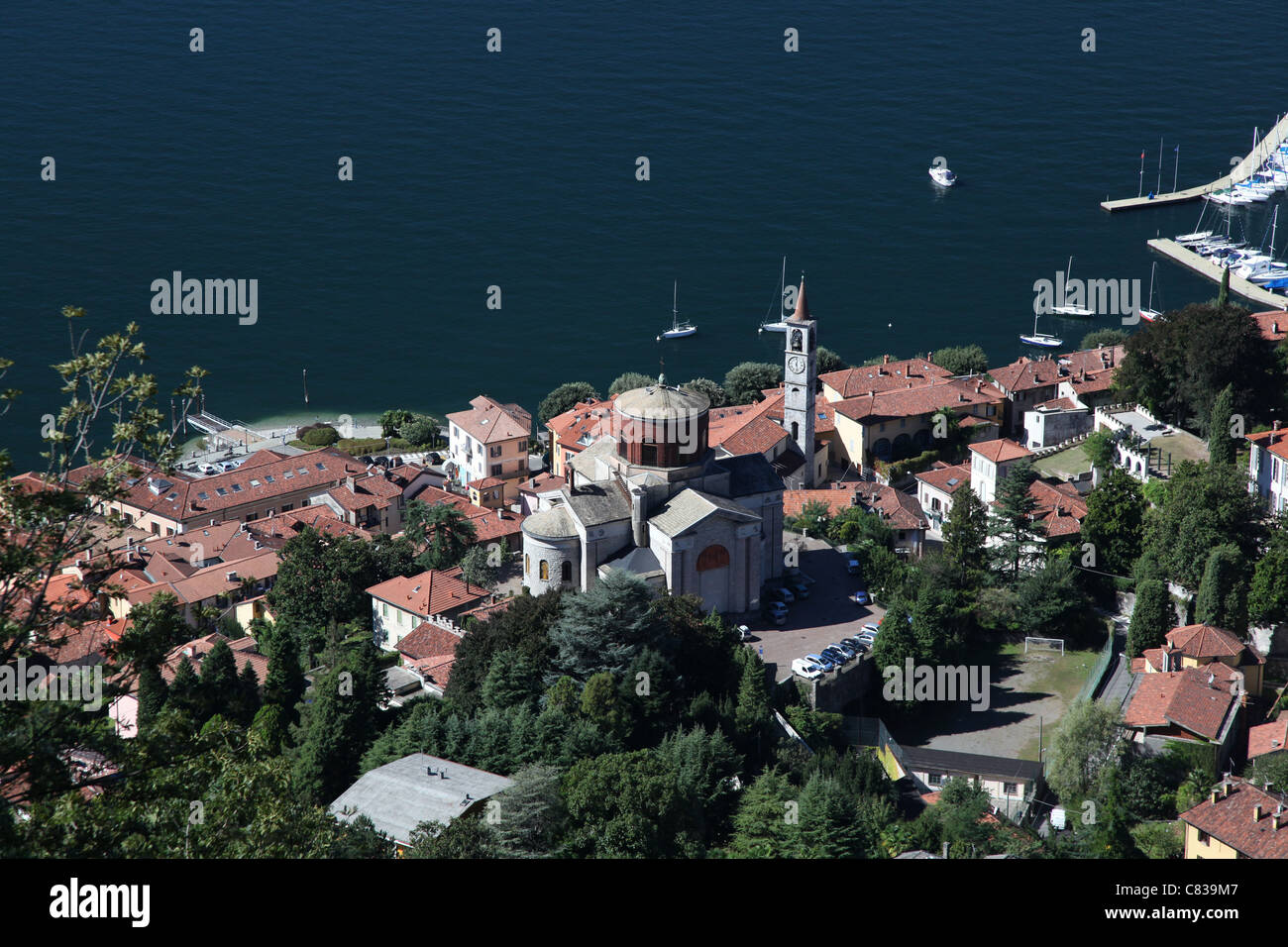Laveno-Mombello und seine beiden großen Kirchen, eine Strecke des Lago Maggiore und einige Boote. Text an der Spitze. Stockfoto