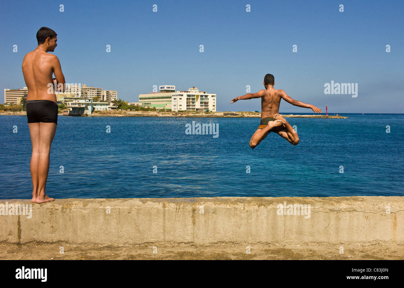 Um der allgegenwärtigen Hitze zu entkommen, sind zwei Jungs im Teenageralter an einem sonnigen Tag entlang des Malecon in Havanna in Bahia De La Habana springen. Stockfoto