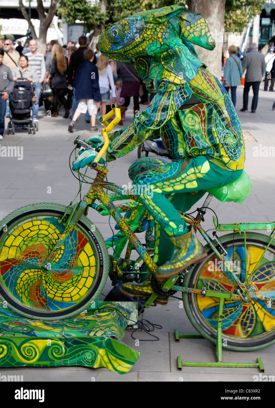 Entertainer, gekleidet wie ein Chamäleon auf einem Fahrrad an Londons South Bank Stockfoto