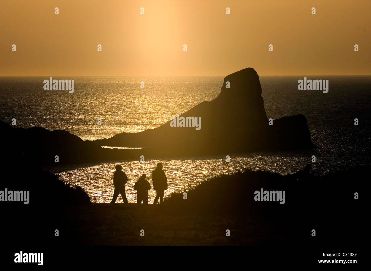 Eine Gruppe von Wanderern den spektakulären Sonnenuntergang über den Würmern Kopf vor der Küste der Gower-Halbinsel im Südwesten von Wales. Stockfoto