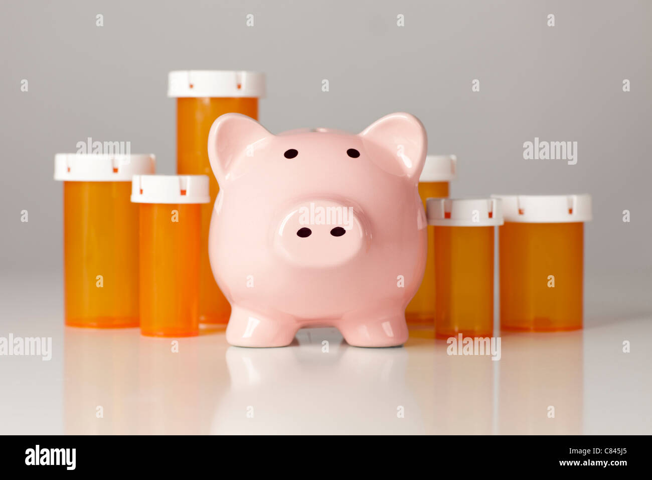 Sparschwein vor mehreren Medizin-Flaschen auf einem abgestuften Hintergrund. Stockfoto