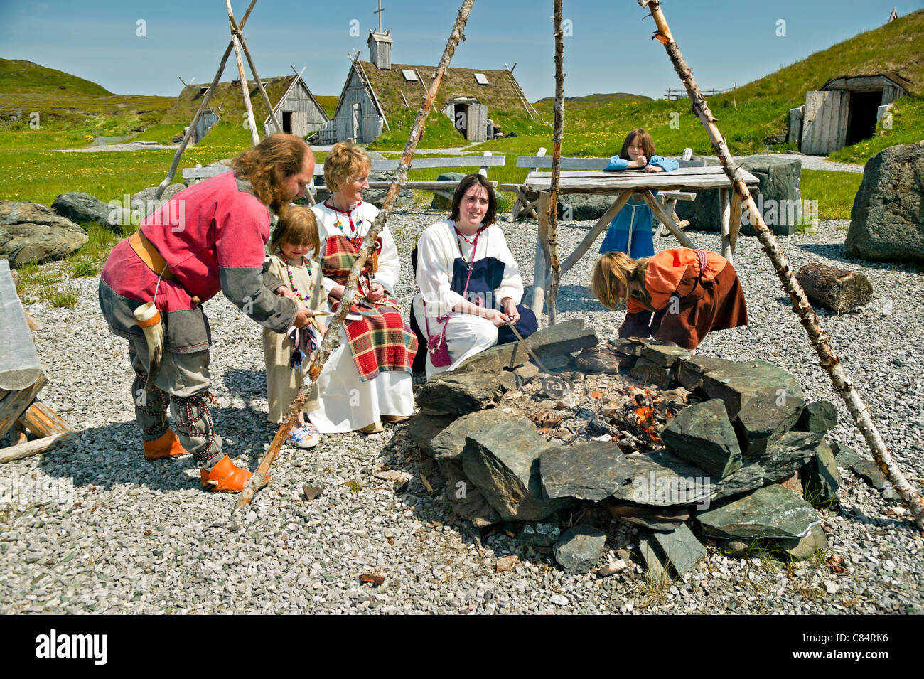 Viking-Familie um eine offene Feuerstelle mit Hütten im Hintergrund Norstead Viking Website, L´Anse-Aux-Meadows, in Newfoudland. Stockfoto