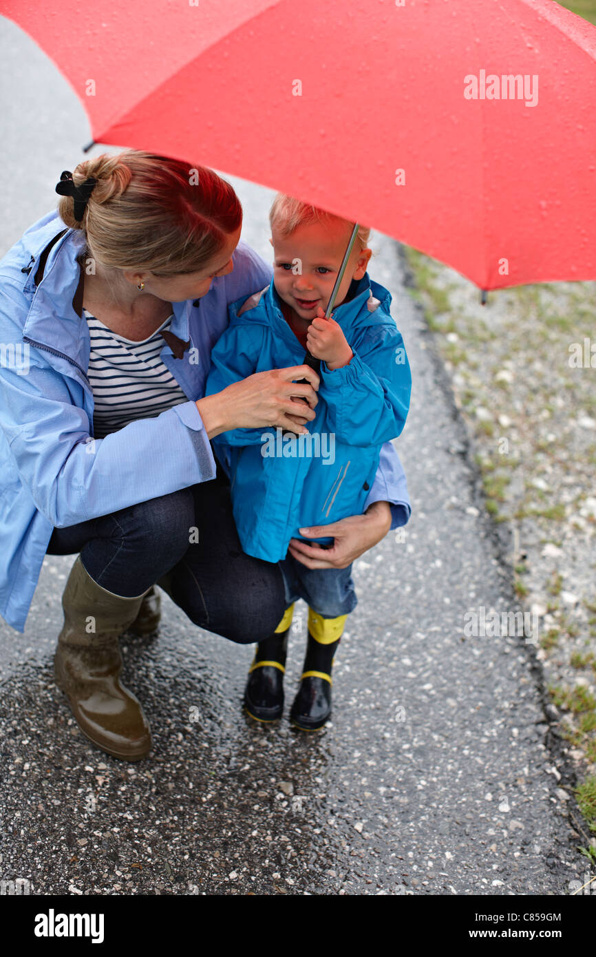 Mutter und Sohn mit Regenschirm auf Straße Stockfoto