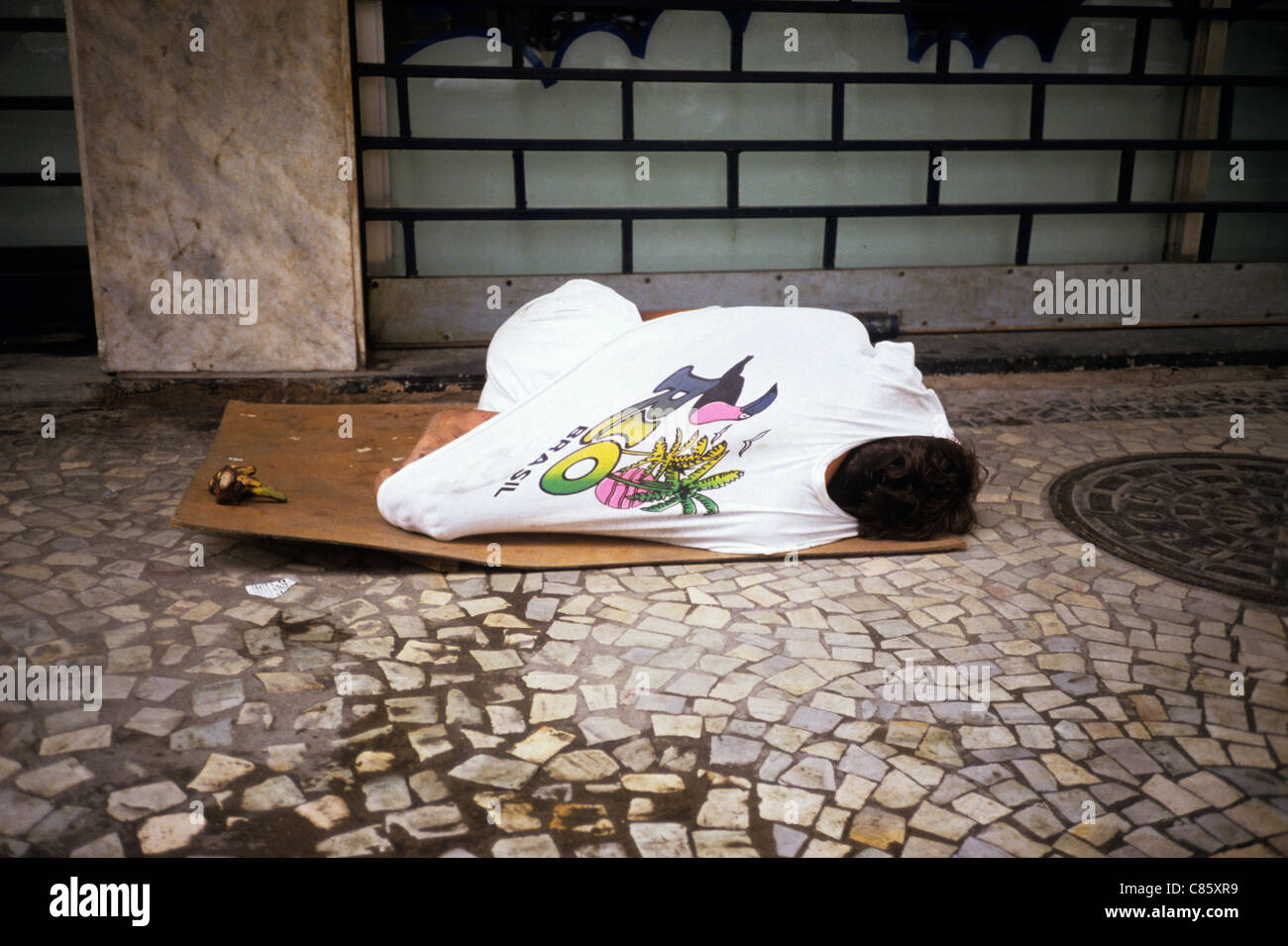 Rio De Janeiro, Brasilien; Kind trägt ein "Rio Brasilien" T-shirt schlafen auf einem Stück Pappe außerhalb eines Gebäudes, verjährt. Stockfoto