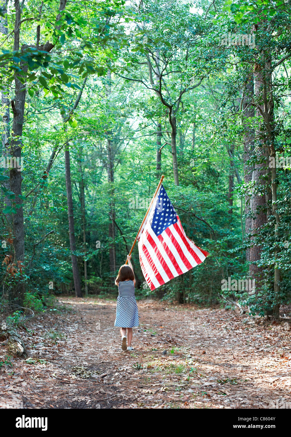 Kleine Mädchen tragen eine amerikanische Flagge durch den Wald Stockfoto