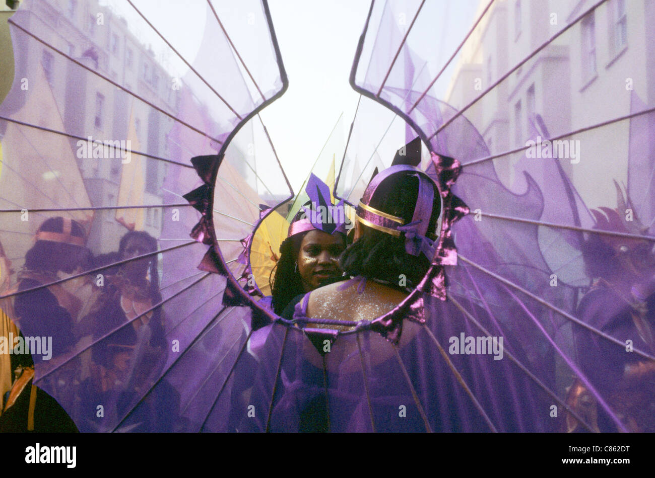 London, England. Notting Hill Karneval, lächelnde Gesichter durch lila Flügel. Stockfoto