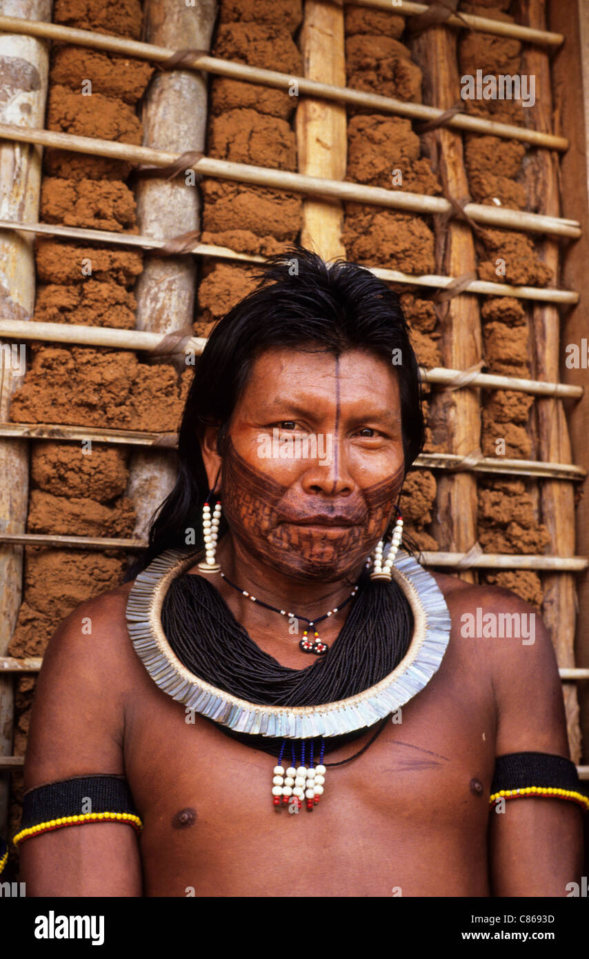 A-Ukre Dorf, Brasilien. Porträt von Kryt, ein Kayapo-Mann mit schwarzem Gesicht malen, Perle und Muschel Schmuck mit Flechtwerk und Lehm Wand. Stockfoto