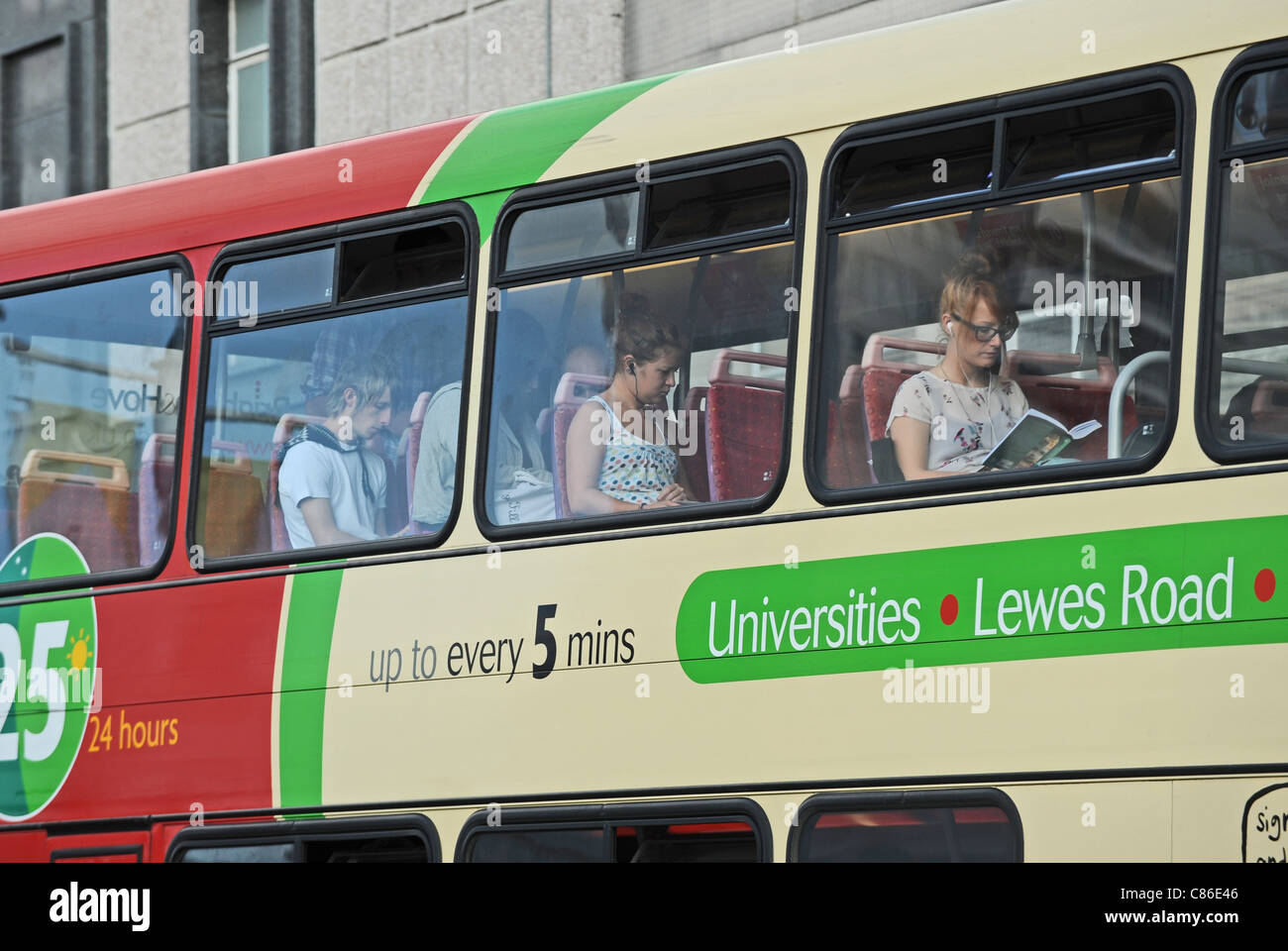 Junge Passagiere sitzen auf Oberdeck lesen und oder Benutzung von Mobiltelefonen auf Text-bus und Musikhören UK Stockfoto