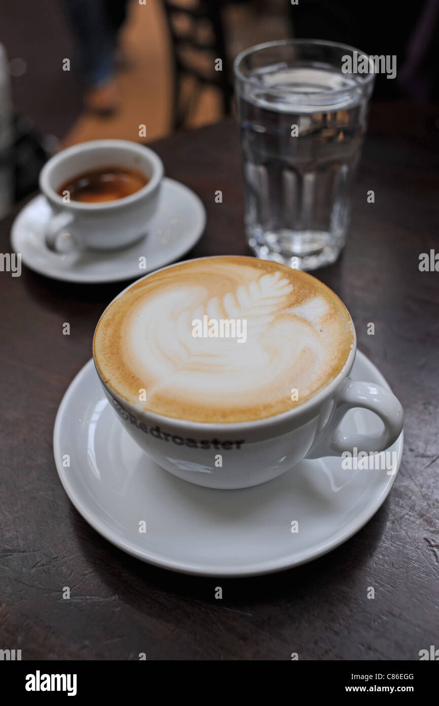 Eine Tasse Cappuccino Kaffee mit einer Feder förmigen Muster auf den Schaum eine Tasse Espresso im Redroaster Café Brighton Stockfoto