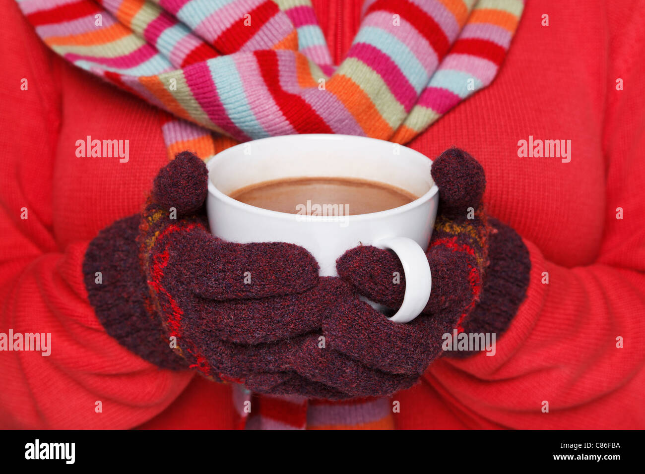 TRIKOTSHIRT Foto einer Frau trägt einen roten Pullover, wollene Handschuhe und Schal hält eine Tasse heiße Schokolade voller Nahaufnahme Stockfoto