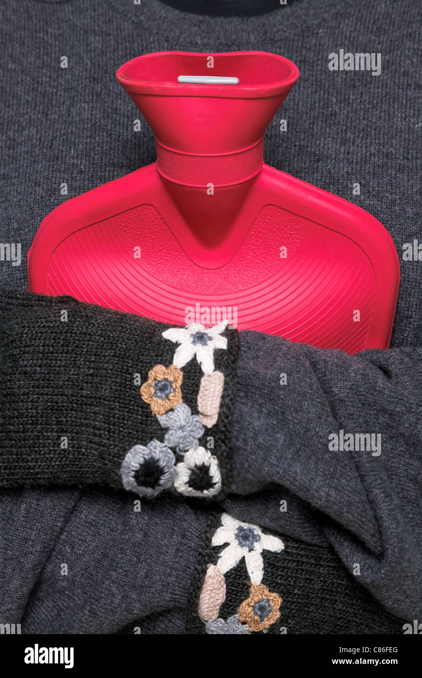 Foto einer Frau mit einer roten Wärmflasche an ihre Brust, während tragen hand Kniited wollene Handschuhe versucht warm zu halten Stockfoto