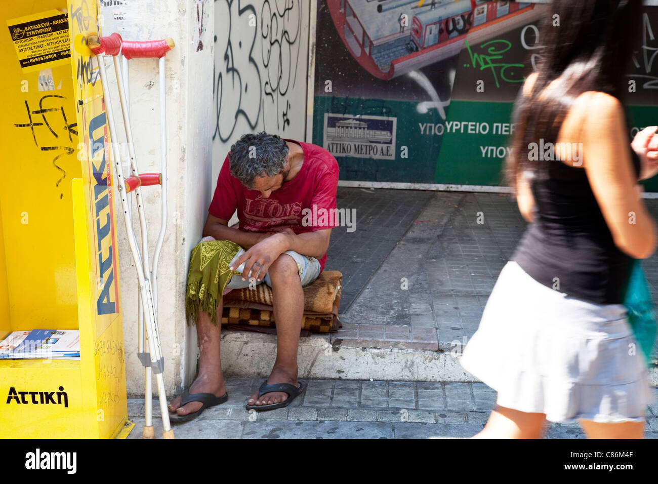 Die Menschen gehen vorbei an einem Obdachlosen auf der Straße in Monastiraki. Die Kluft zwischen Arm und Reich in Athen ein alltäglicher Anblick. Stockfoto