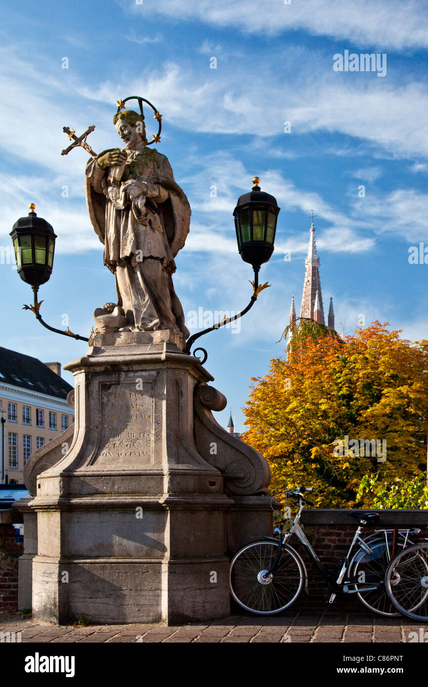 Statue von St. Johannes von Nepomuk, Sint-Jan Nepomucenus auf Wollestraat Brücke in Brügge. Turm der Kirche unserer lieben Frau im Hintergrund. Stockfoto