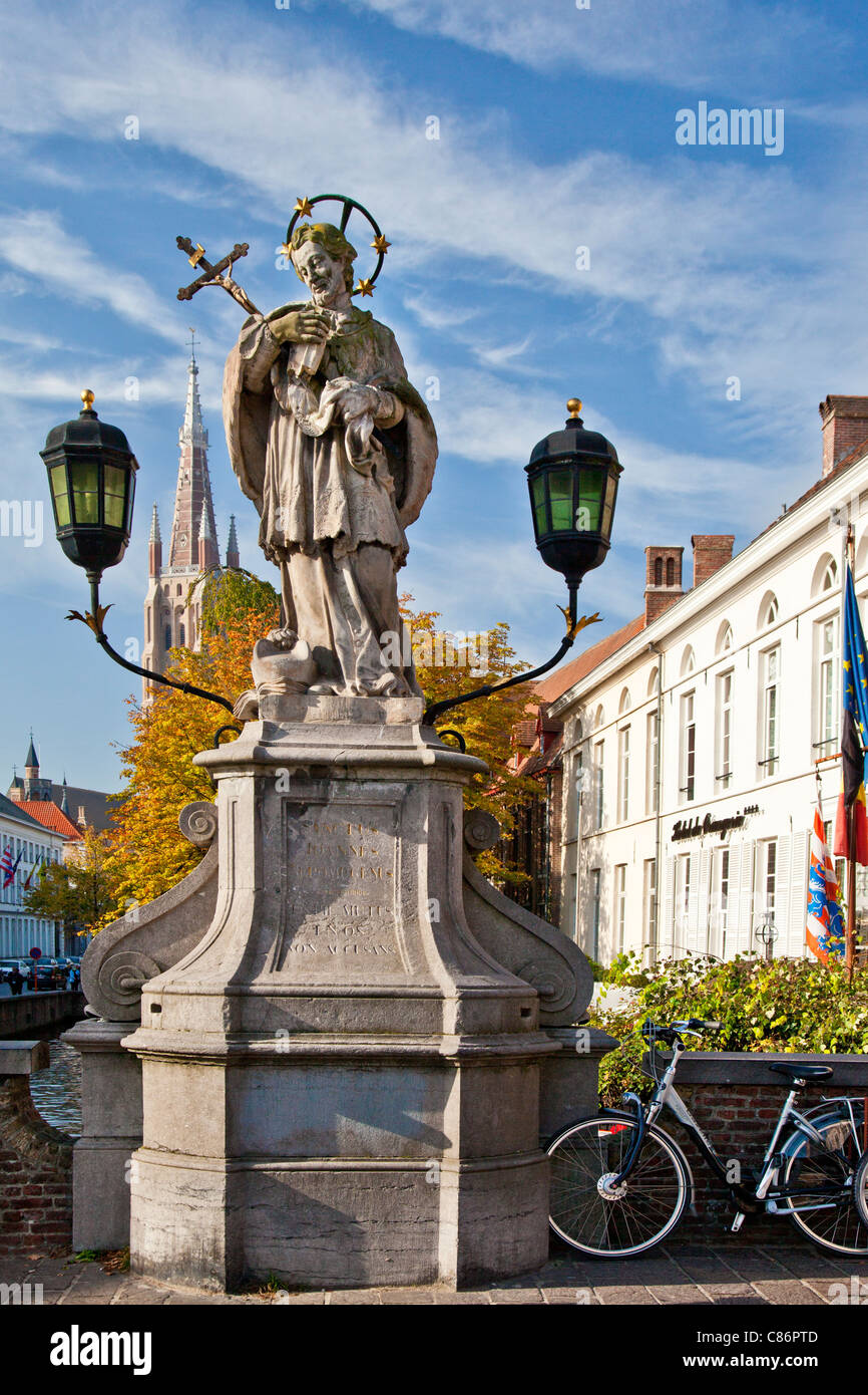 Statue von St. Johannes von Nepomuk, Sint-Jan Nepomucenus auf Wollestraat Brücke in Brügge. Turm der Kirche unserer lieben Frau im Hintergrund. Stockfoto
