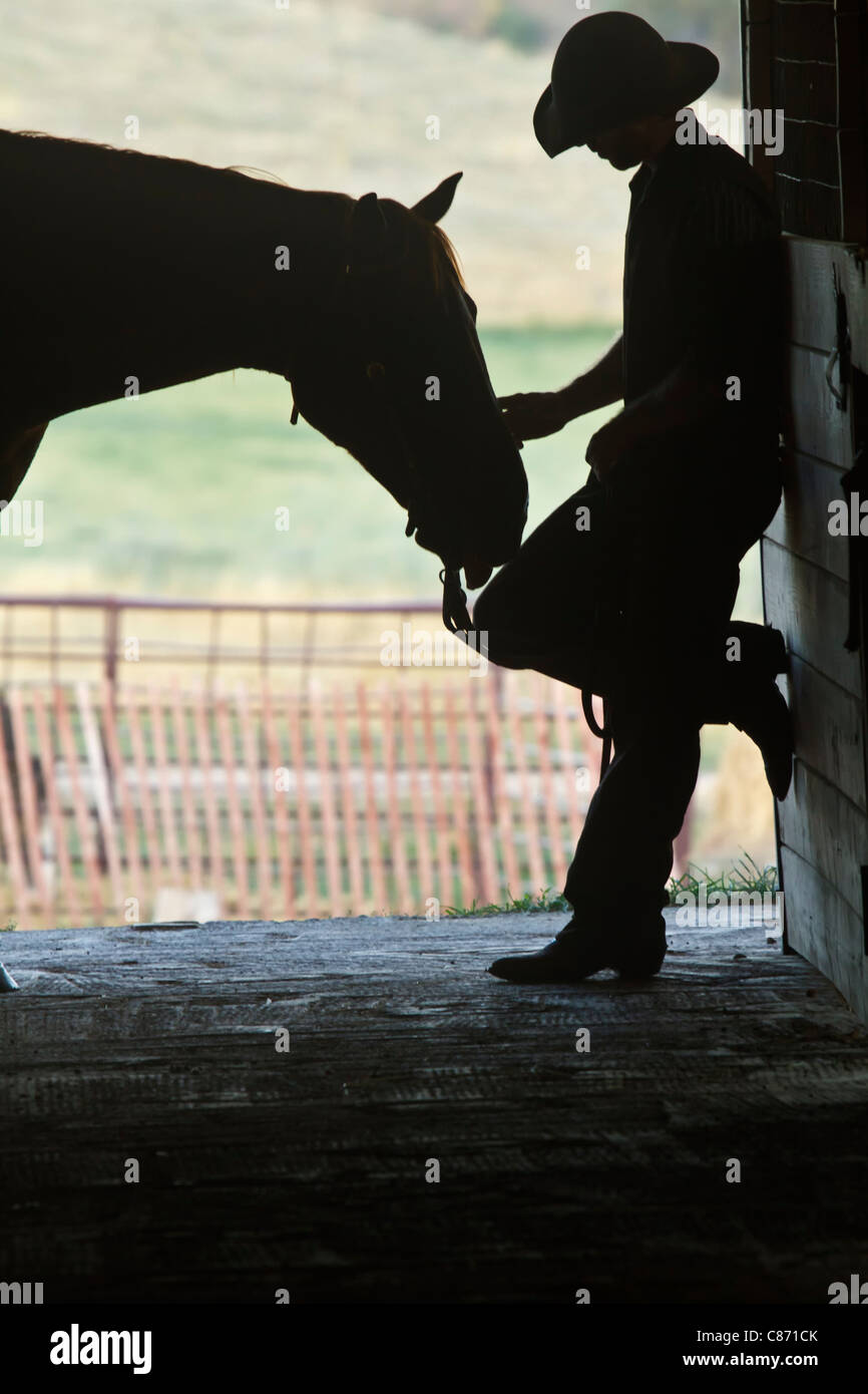 Cowboy lehnt sich gegen den Stall Pferd streicheln sein Pferd in der silhouette Stockfoto