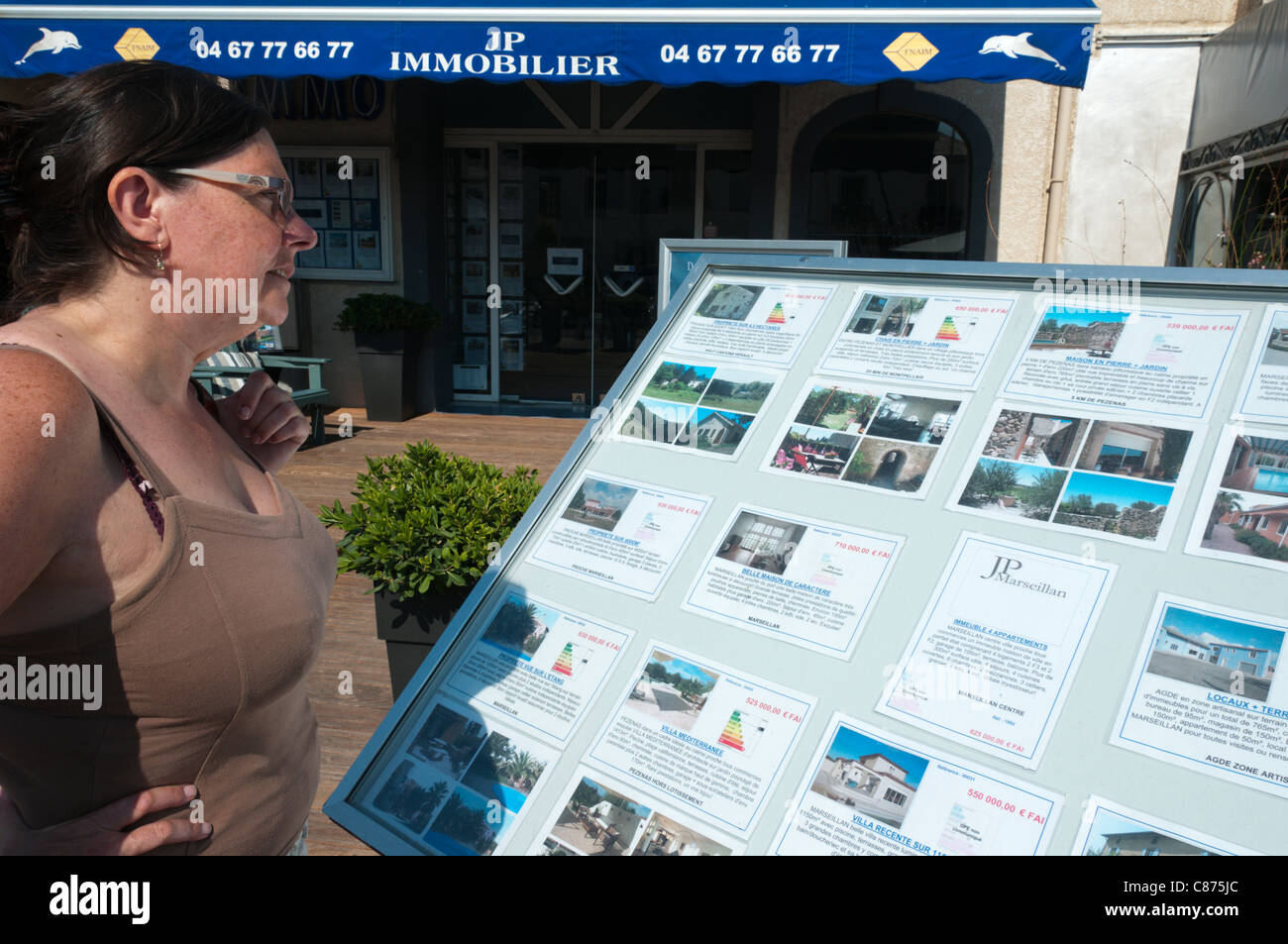 Eine Frau schaut Details zu Ferienhäuser zum Verkauf oder zur Miete außerhalb eines Immobilienmakler in Marseillan, Südfrankreich. Stockfoto