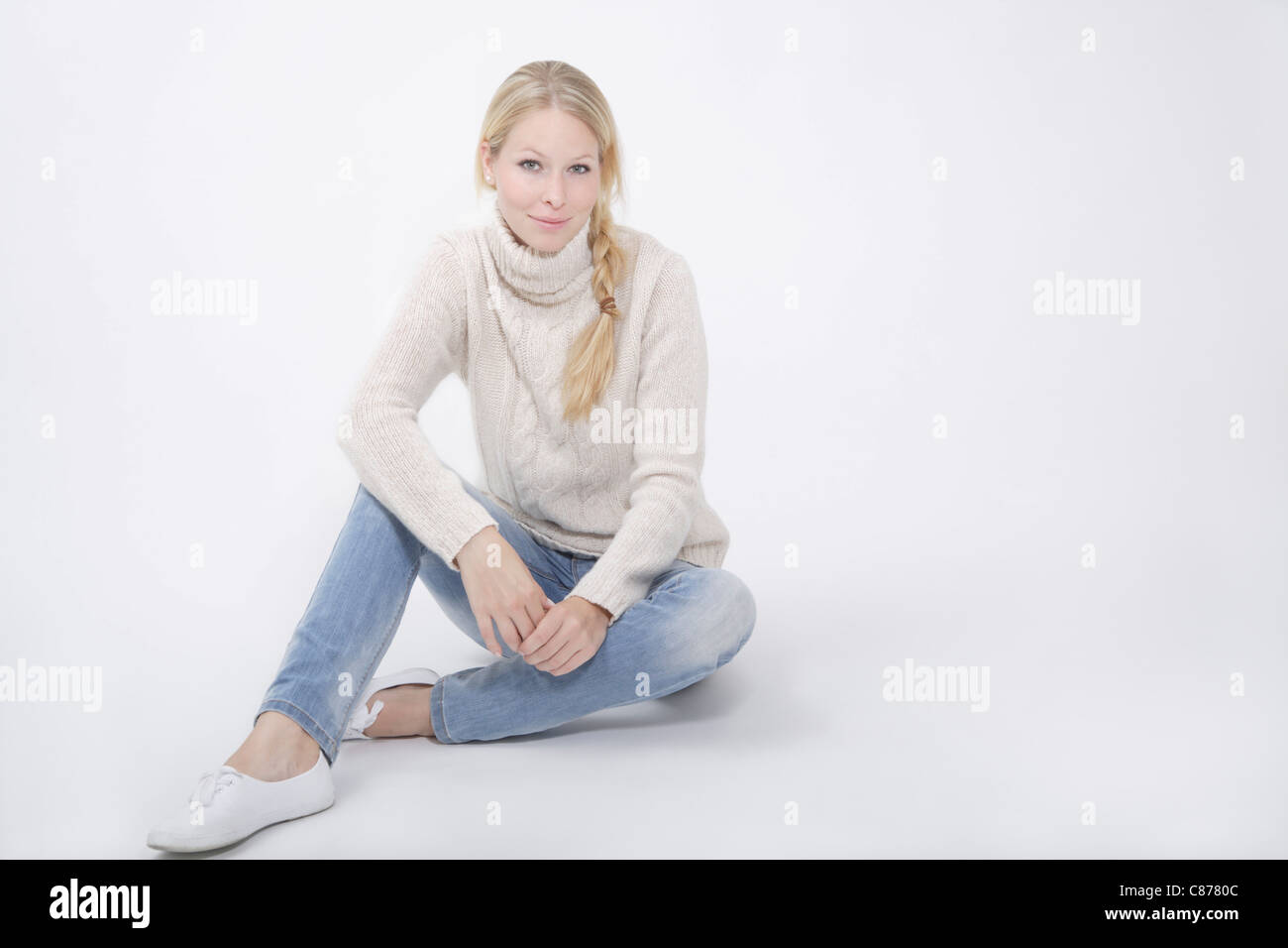 Junge Frau tragen Tutleneck Jumper sitzt auf weißem Hintergrund, Lächeln, Porträt Stockfoto