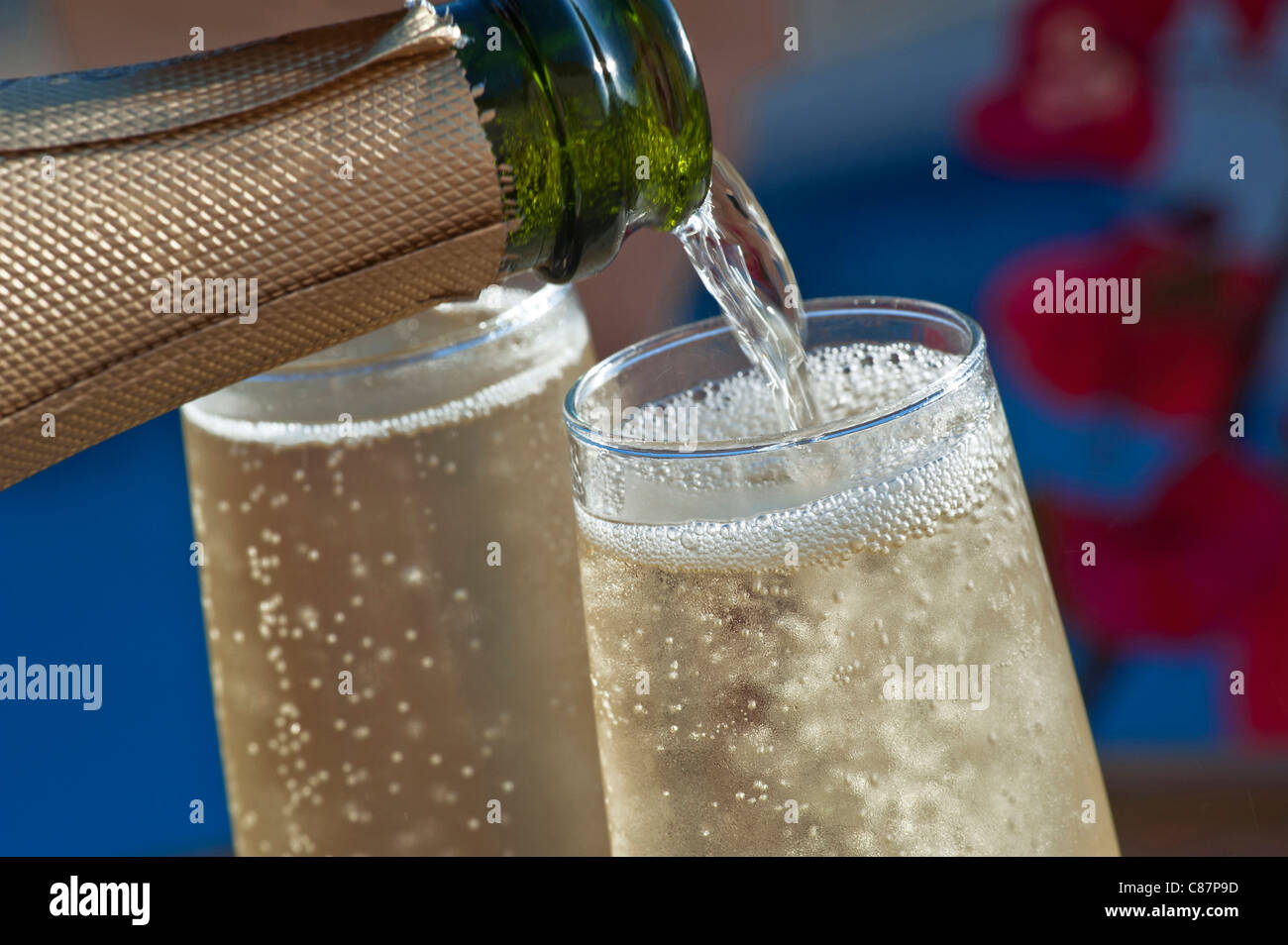 Champagner Sekt Gießen im Freien Nahaufnahme gekühlte Gläser Wein auf der sonnigen Terrasse mit Bougainvillea Blumen und Schwimmbad im Hintergrund Stockfoto