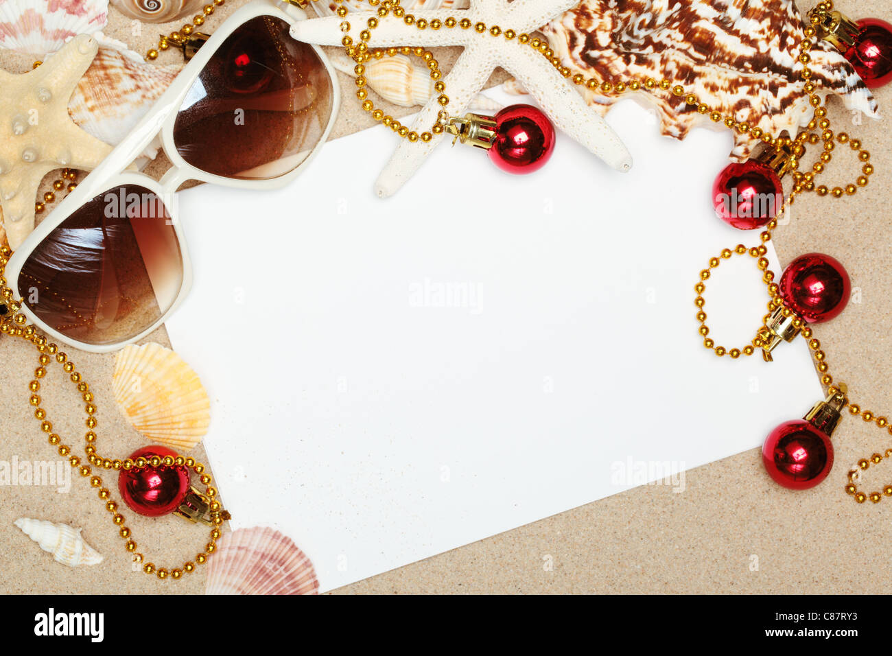 Weihnachtskugeln, Sonnenbrillen und leere Karte am Sandstrand, Nahaufnahme. Stockfoto