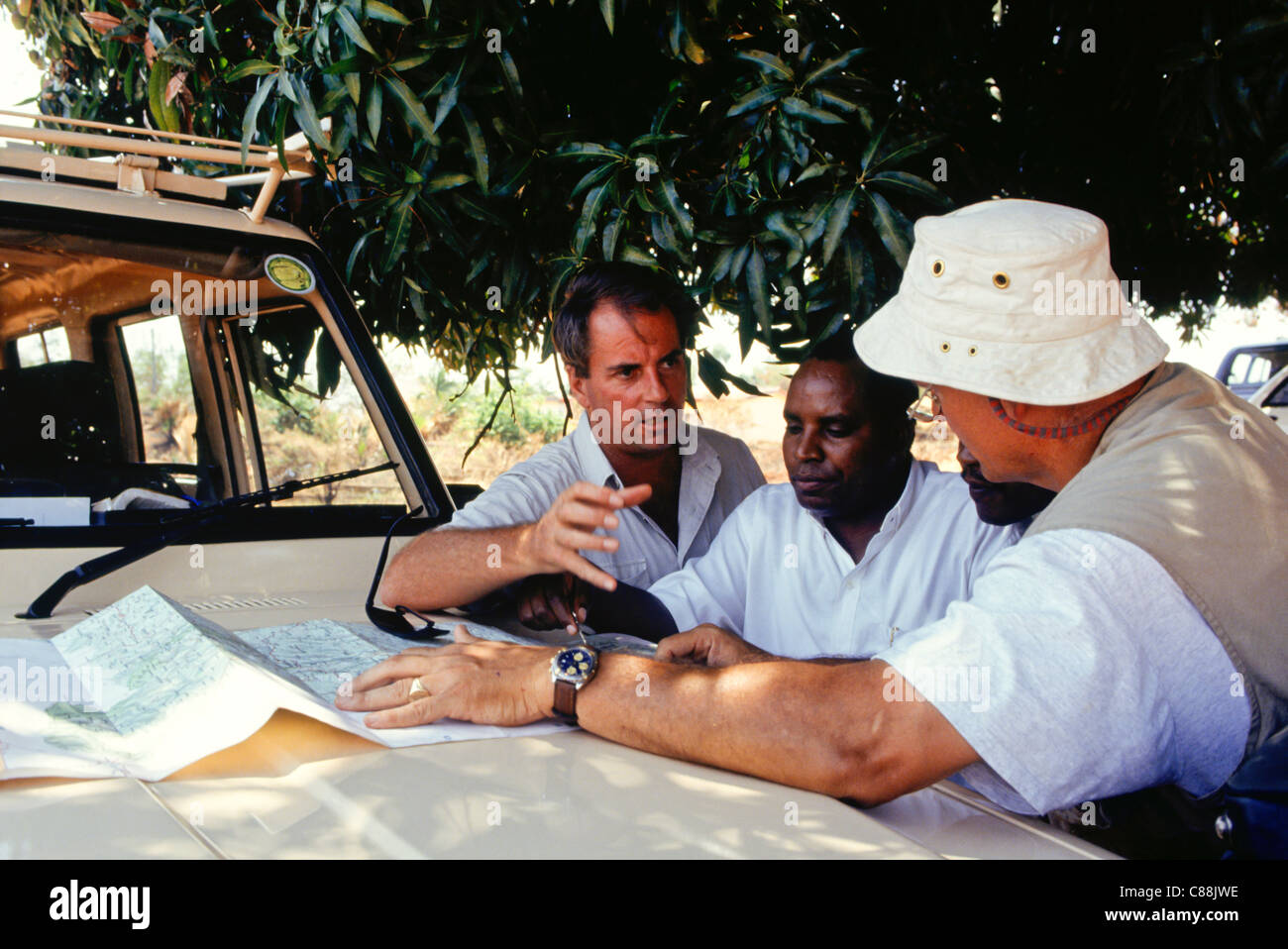 Gombe, Tansania. Gruppe von Touristen auf Safari Blick auf eine Karte, auf der Motorhaube ein Allradfahrzeug. Stockfoto