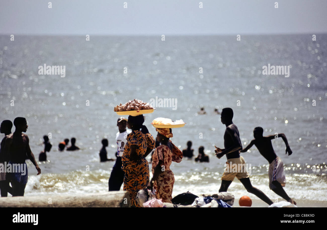 Libreville, Gabun. Menschen am Strand und im Meer, sonniges Wochenende; Frauen, die die Snacks zum Verkauf auf Tabletts auf ihren Köpfen. Stockfoto