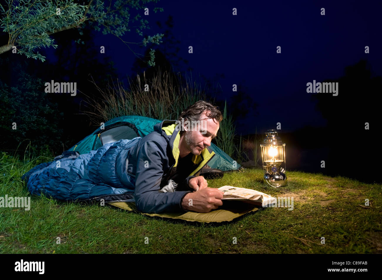 Deutschland, Bayern, Ammersee, Mann Lesebuch in der Nähe von Seeufer beim camping in der Nacht Stockfoto