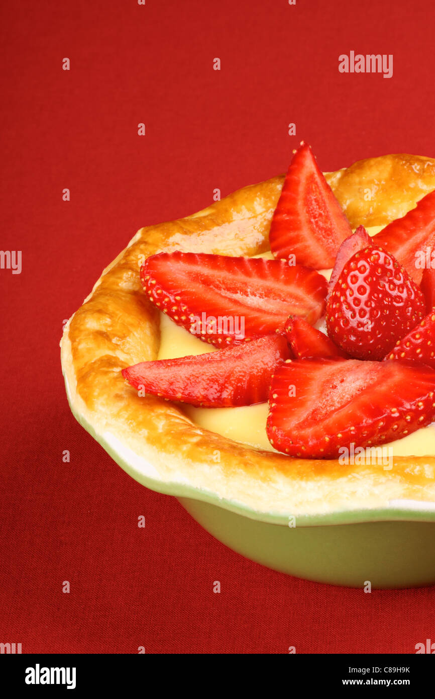 Erdbeeren und Vanillecreme Torte in einer grünen Auflaufform auf einem roten Hintergrund. Stockfoto