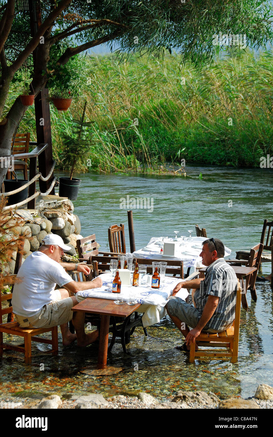 AKYAKA, TÜRKEI. Zwei Männer trinken Bier / im Fluss Azmak mit der Gökova Conservation Area hinter. 2011. Stockfoto