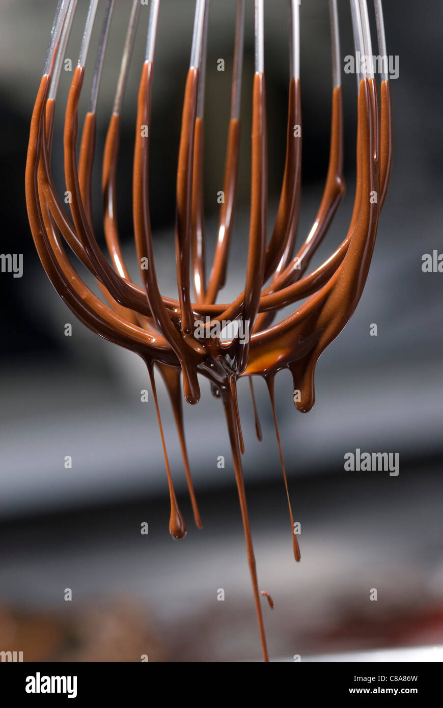 Geschmolzene Schokolade tropft aus einem Schneebesen Stockfoto