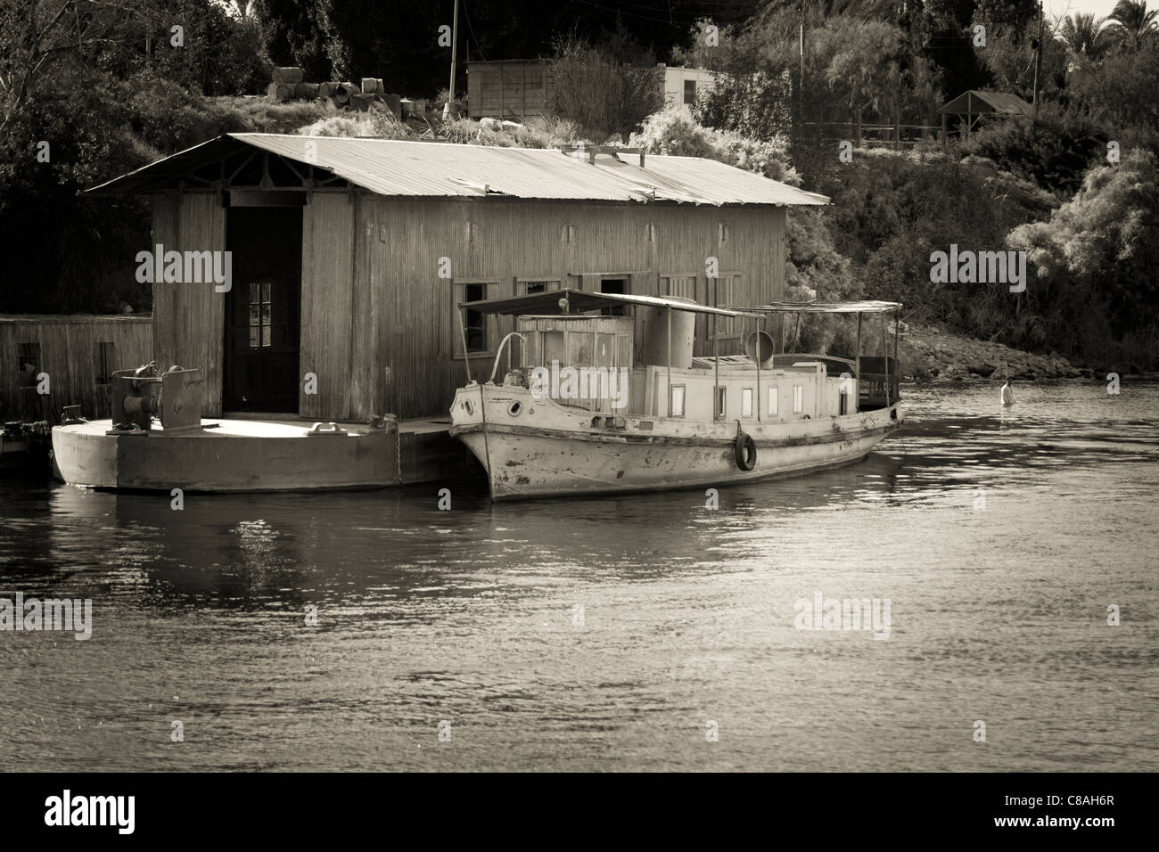 Monochrome Schuss von Nil-Ufer mit kleinen, vereinzelt Spritztülle Boot ankern neben schwimmenden Halle Mann Baden in der Nähe, Ägypten Stockfoto