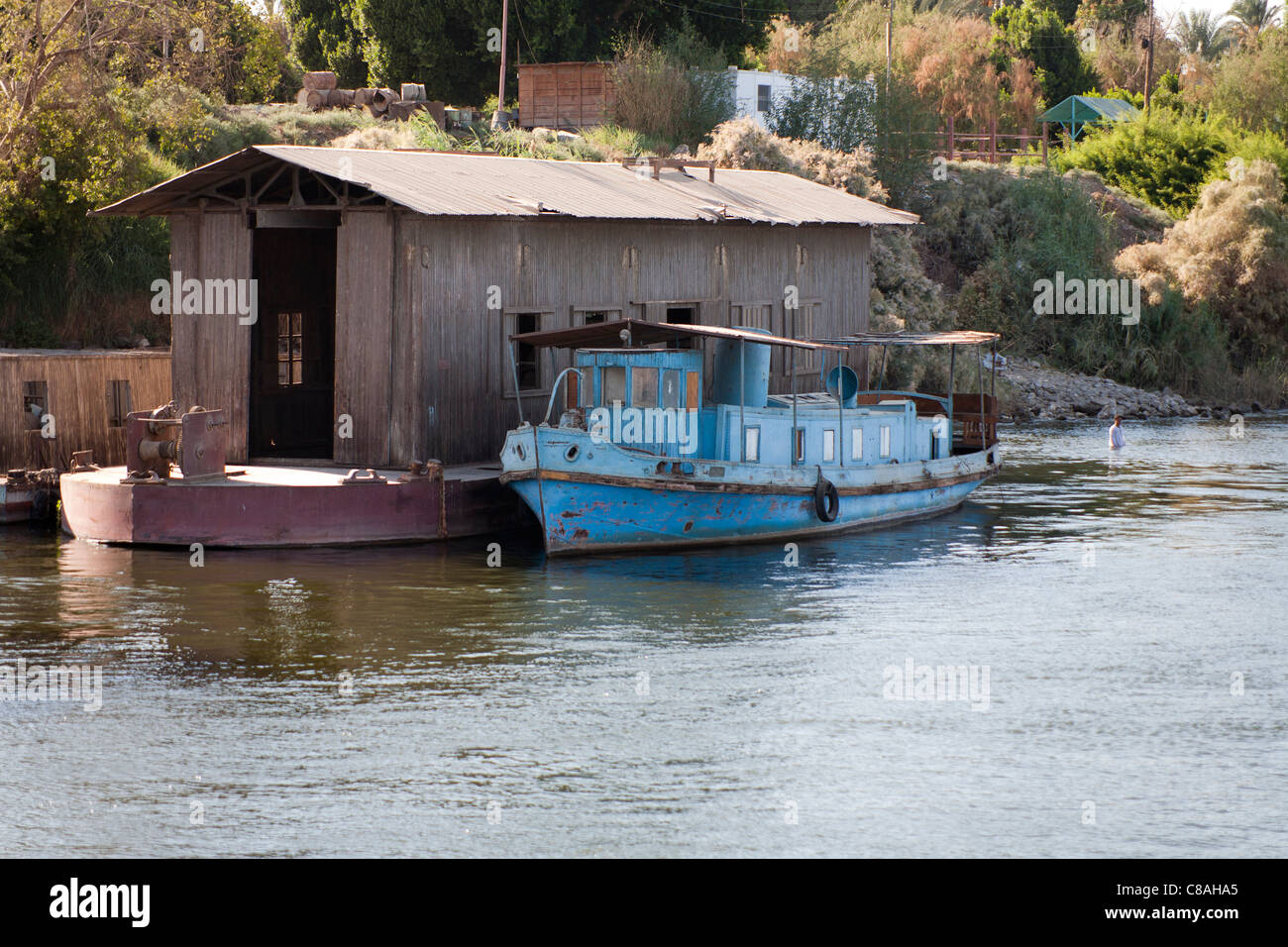 Nil-Ufer mit kleinen blauen, vereinzelt Spritztülle Boot ankern neben braun schwimmenden Halle, Mann, Baden in der Nähe, Ägypten Stockfoto