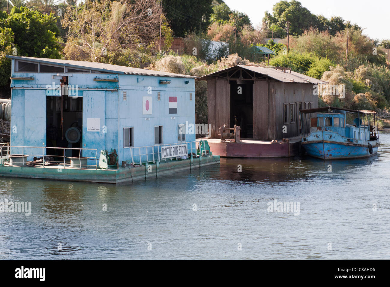 Nil-Ufer mit kleinen blauen, vereinzelt Spritztülle Boot ankern neben Schuppen, schwimmende Pumpstation im Vordergrund Stockfoto