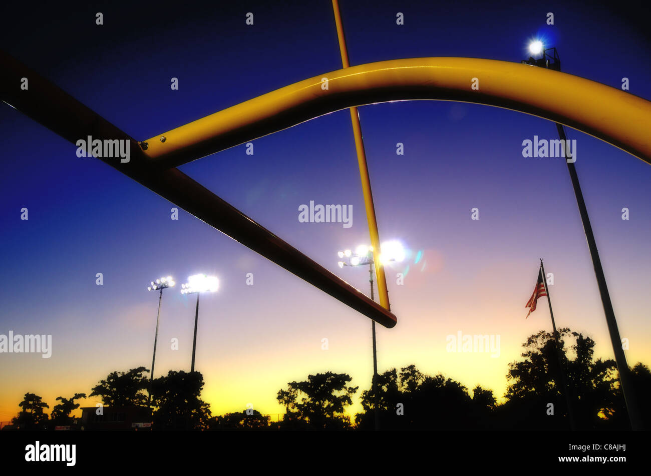 US-amerikanischer American-Football Torpfosten in der Abenddämmerung mit Silhouette Baumgrenze und US-Flagge Stockfoto