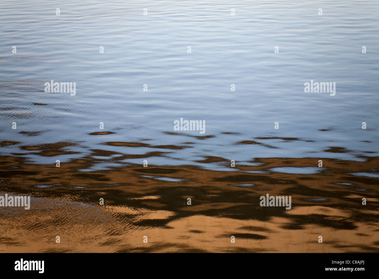 Reflexionen im beweglichen Flusswasser erstellen abstrakte Muster in braun und blues Stockfoto