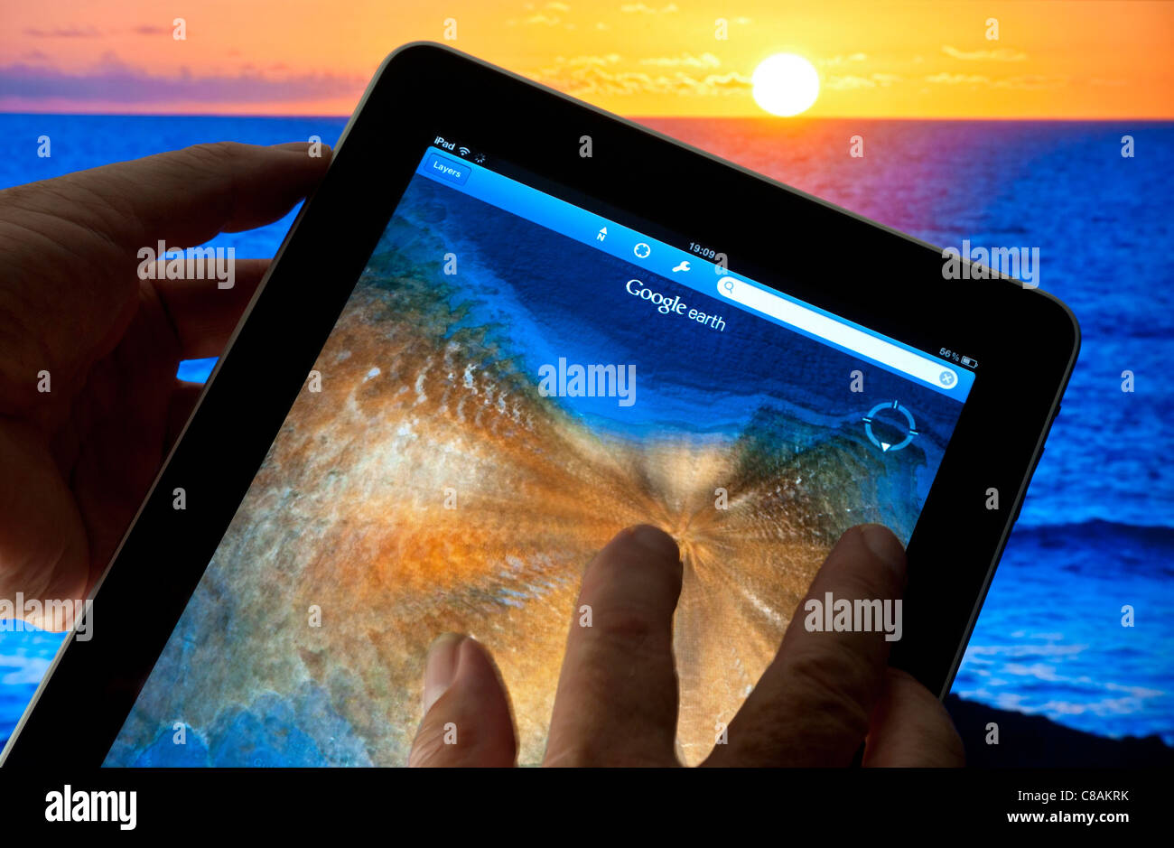 Touchscreen Apple iPad mit Finger auf Touchscreen zoomen Smart Tablet mit Google Earth Anwendung auf dem Display, Sonnenuntergang und Meer im Hintergrund, Stockfoto