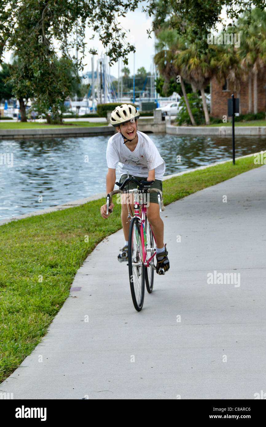 Ein behinderter jungen Mann lächelt und fährt Fahrrad entlang einer Marina in St. Petersburg, Florida. Stockfoto