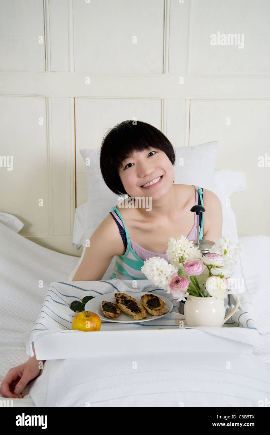 Junge Frau im Bett zu frühstücken Stockfoto