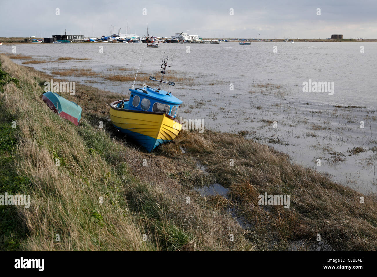 kleine gelbe und blaue Fischerboot aufgegeben am Ufer des Flusses Alde bei Slaughden, in der Nähe von Aldeburgh, Suffolk, UK Stockfoto