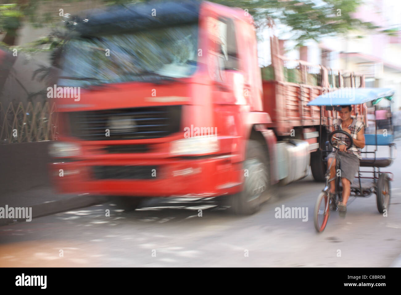 Ein Bicitaxi (Fahrrad-Taxi) und roten Lieferwagen in der High Street von Holguin, Kuba. Stockfoto