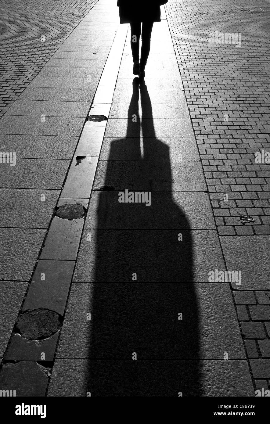 Frau zu Fuß auf dem Bürgersteig mit tiefstehende Sonne wirft lange Schatten Stockfoto