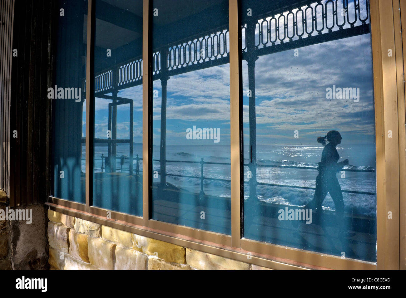 © Tony Bartholomew reflektiert ein Jogger am frühen Morgen in einem Fenster direkt am Meer in der Nähe von Scarborough Spa, an der Stadt South Bay Stockfoto