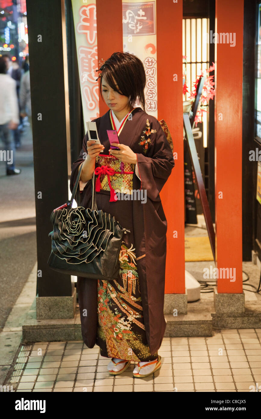 Japan, Tokio, Roppongi, junges Mädchen im Kimono mit zwei Handys Stockfoto