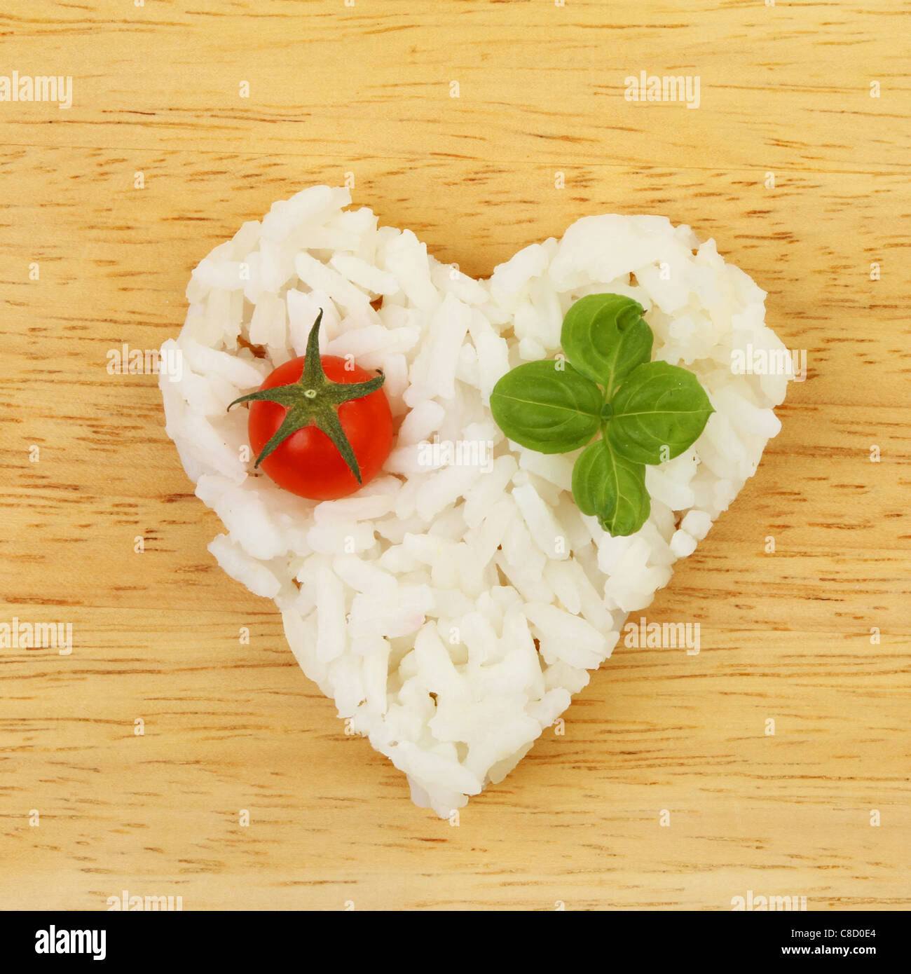 Gesunde Ernährung, Reis in Form eines Herzens mit Tomaten und Basilikum auf einem Holzbrett Stockfoto