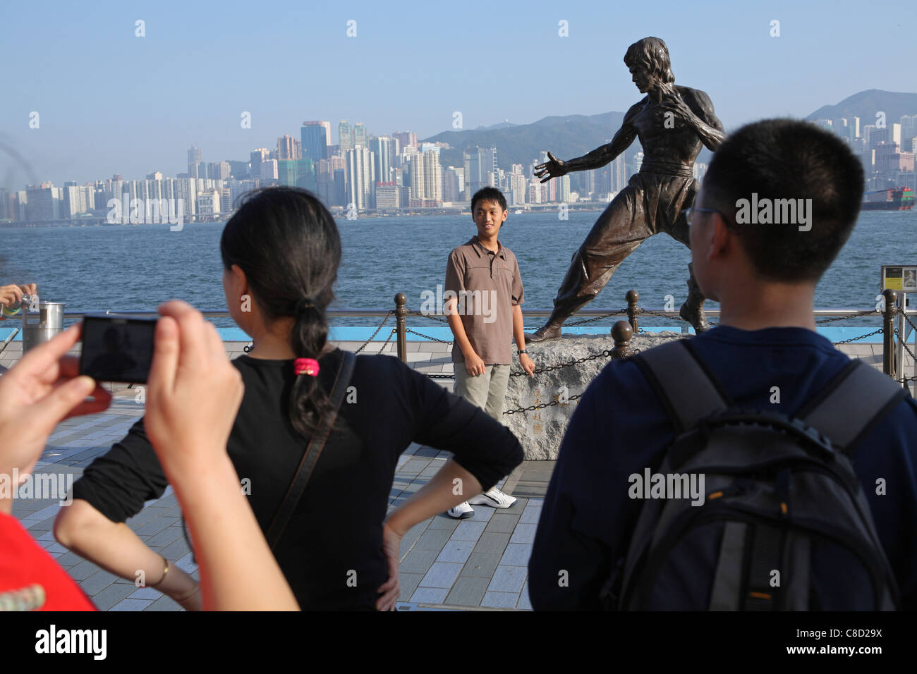 Touristen posieren für Fotos von Statue der Hong Kong Martial Arts und Filmstar Bruce Lee (1940-73) auf der Avenue of the Stars Stockfoto