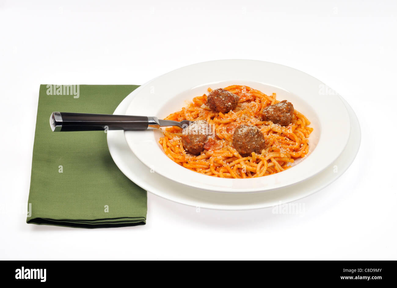 Eine Portion Spaghetti und Fleischbällchen garniert mit Käse in einer weißen Schüssel mit Löffel und grünen Serviette auf weißem Hintergrund. Stockfoto